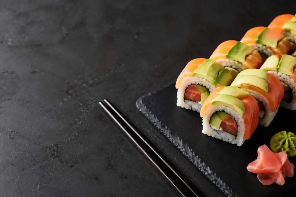 Assorted nigiri and maki sushi arranged on a black slate board with wasabi and pickled ginger