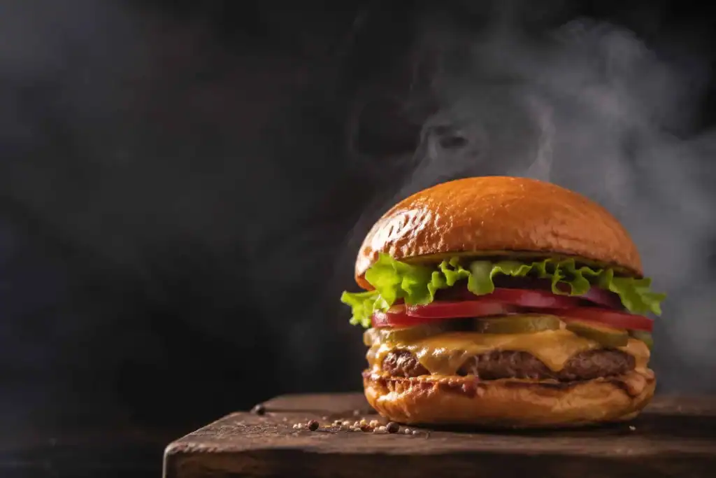 Stacked gourmet beef burger with melted cheese and fresh lettuce on a dark restaurant table